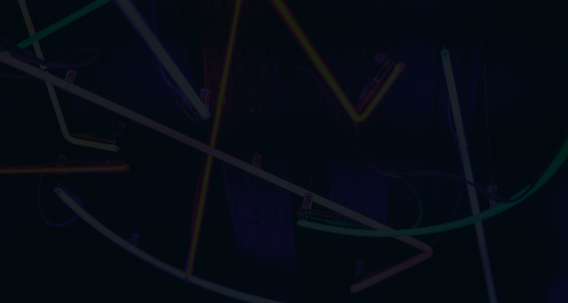 An abstract, dark background with neon lines in various colors creating a network of geometric shapes and angles, giving the impression of a modern, artistic light installation or the visualization of a complex, interconnected system.