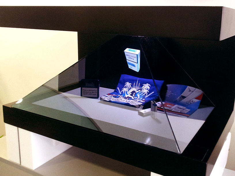 Ugaoni prikaz muzejske vitrine osvetljene iznutra, koja prikazuje holografsku projekciju plavo-belog digitalnog artefakta, kombinujući tradicionalne izložbene metode sa savremenom tehnologijom.
